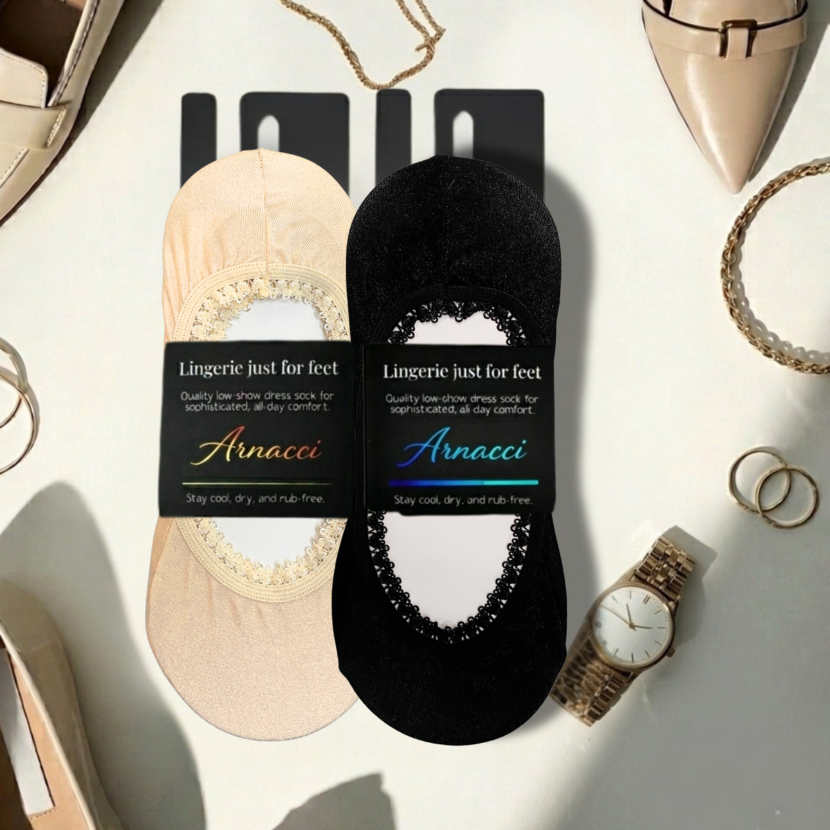 Two pairs of Arnacci Lingerie just for feet socks displayed on black cards, one in beige with a lace trim and one in black with a rhinestone arch, styled on a white surface with fashion accessories.
