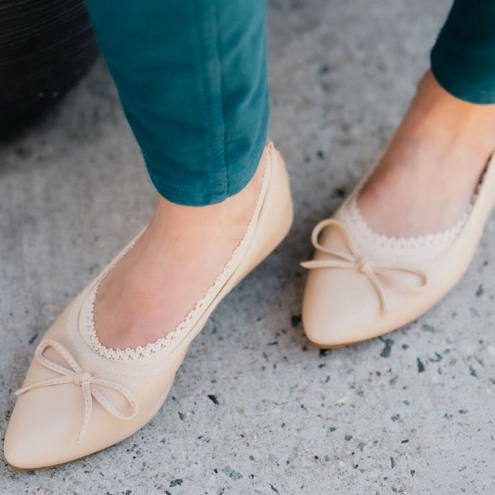 Close-up of Arnacci nude shimmer stretch no show sock in pointed-toe ballerina flats with bow detail, worn with teal pants on a concrete walk.