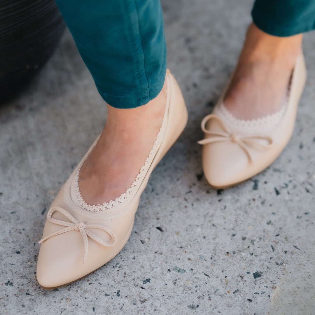 Close-up of a person wearing nude pointed-toe ballet flats with bows, featuring a Sand-colored Arnacci liner that blends perfectly with the shoe and skin for an invisible fit.