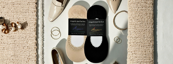 Black and sand shimmer lace no-show footies displayed overhead with heels, jewelry, and accessories, showing luxe trim and stay-put design for dress shoes.