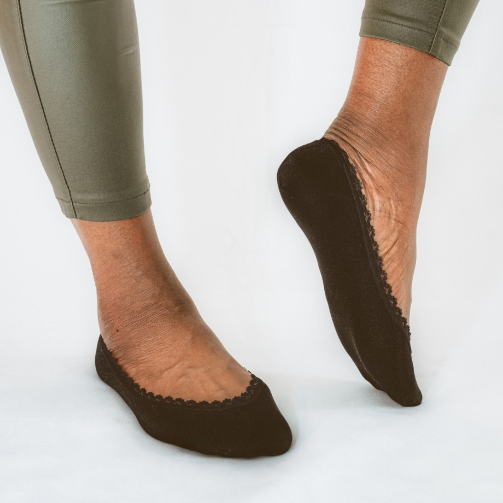 Black shimmer lace no-show footies worn on bare feet, showing non-slip fit and delicate picot lace trim that peeks slightly in flats and heels