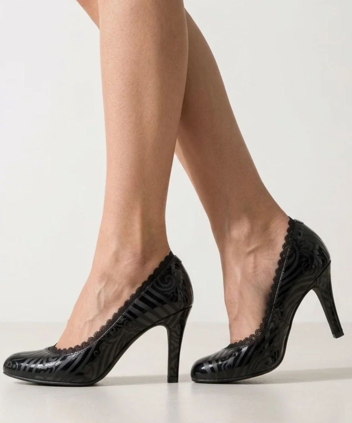 Side view of model's legs wearing Arnacci black lace-trimmed no-show liner socks peeking out from high-heeled black patent shoes with a subtle striped pattern.
